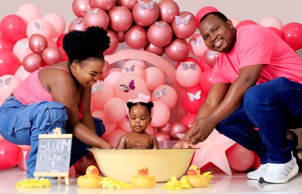 Parents smiling as their baby daughter splashes in a tub at her first-birthday shoot