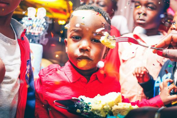 A boy in a red shirt being offered a forkful of cake under falling confetti