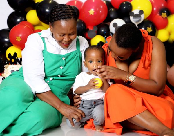 A grandmother and mother laughing with a baby at a Mickey Mouse first birthday